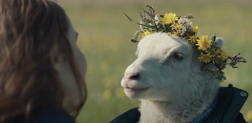 a woman looking at a lamb in a flower crown