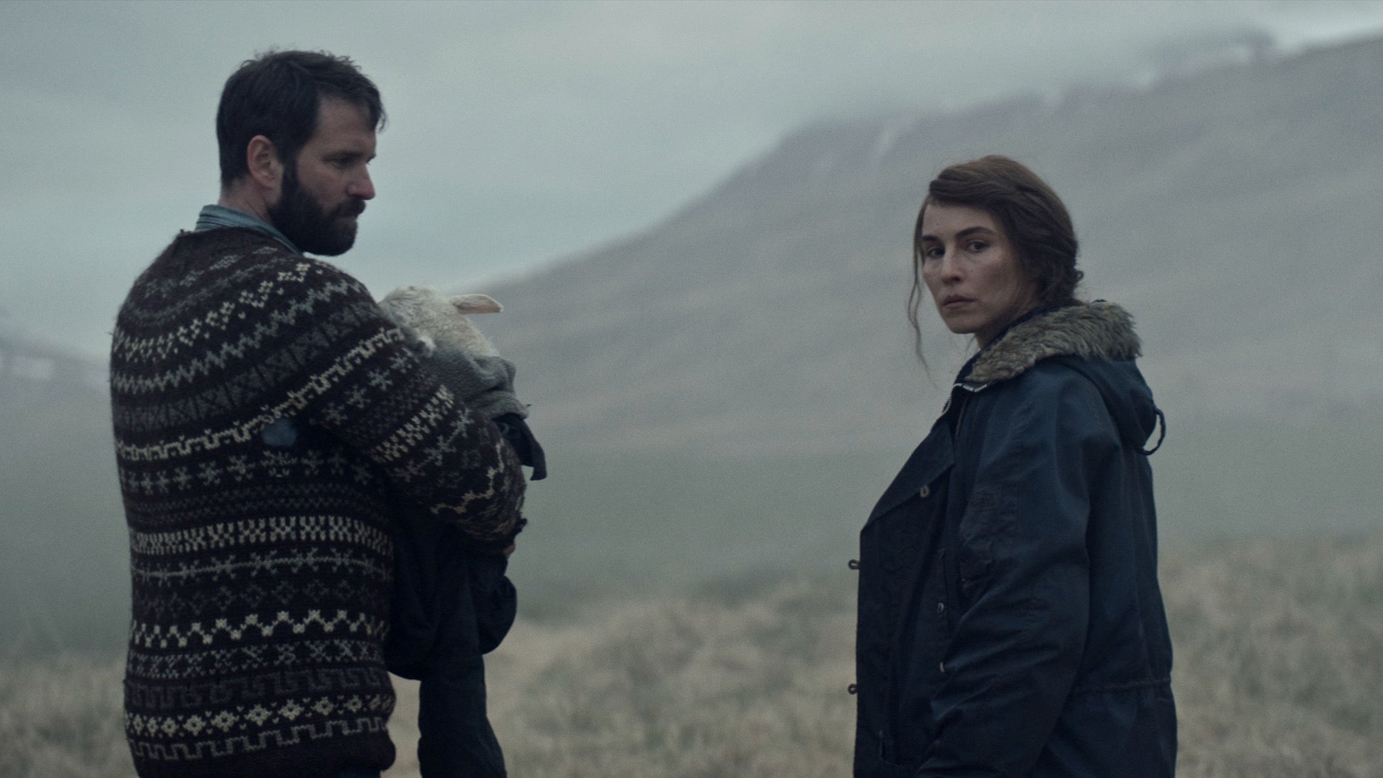 man holding lamb-human hybrid while woman looks over her shoulder