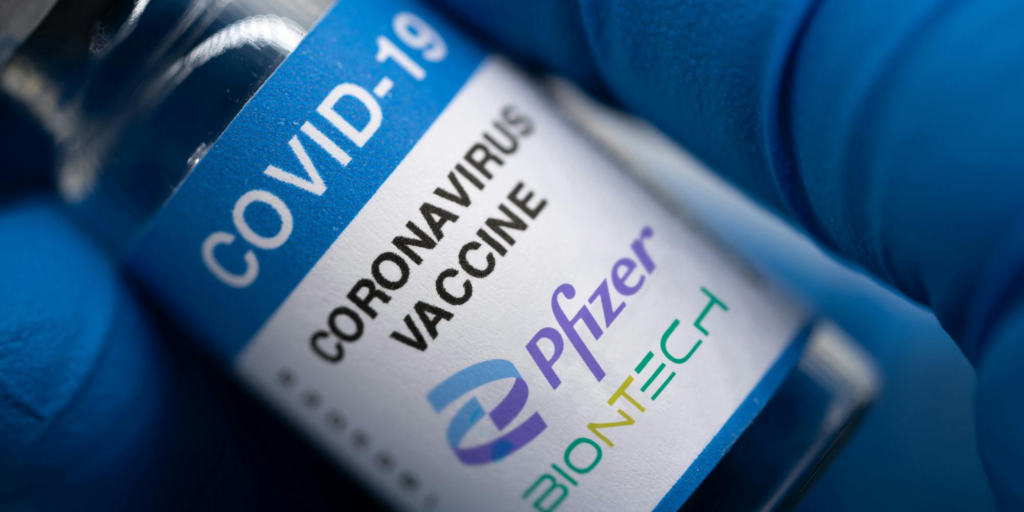 Covid-19 vaccine with Pfizer logo. Doctor's hand holds a bottle with a coronavirus vaccine on a white background.
