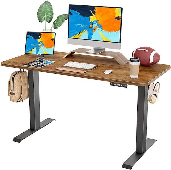 Wood raising desk with two computer monitors, a football, coffe, keyboard, and other knicknacks on the surface