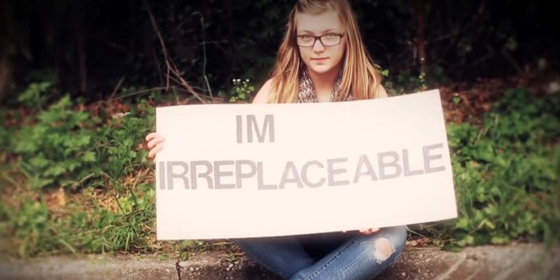 Gabby Petito in a music video. She is holding a sign that says 'I'm Irreplaceable.'