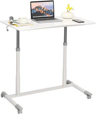 White raised standing desk with computer, lamp, mug, phone, and writing utensils on the surface. The perfect starter desk for a home office setup