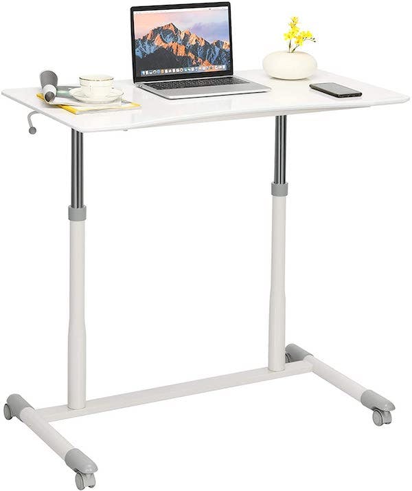 White raised standing desk with computer, lamp, mug, phone, and writing utensils on the surface