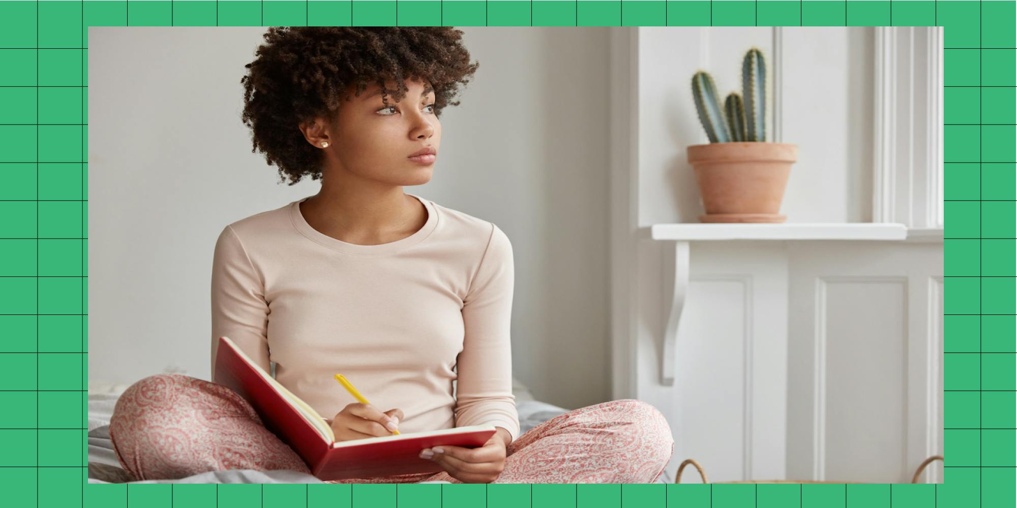 Cropped shot of dark skinned woman sits crossed legs, wears pyjamas, makes notes in diary, focused aside, blank copy space against domestic interior. Blogger creats publication for blog in notebook