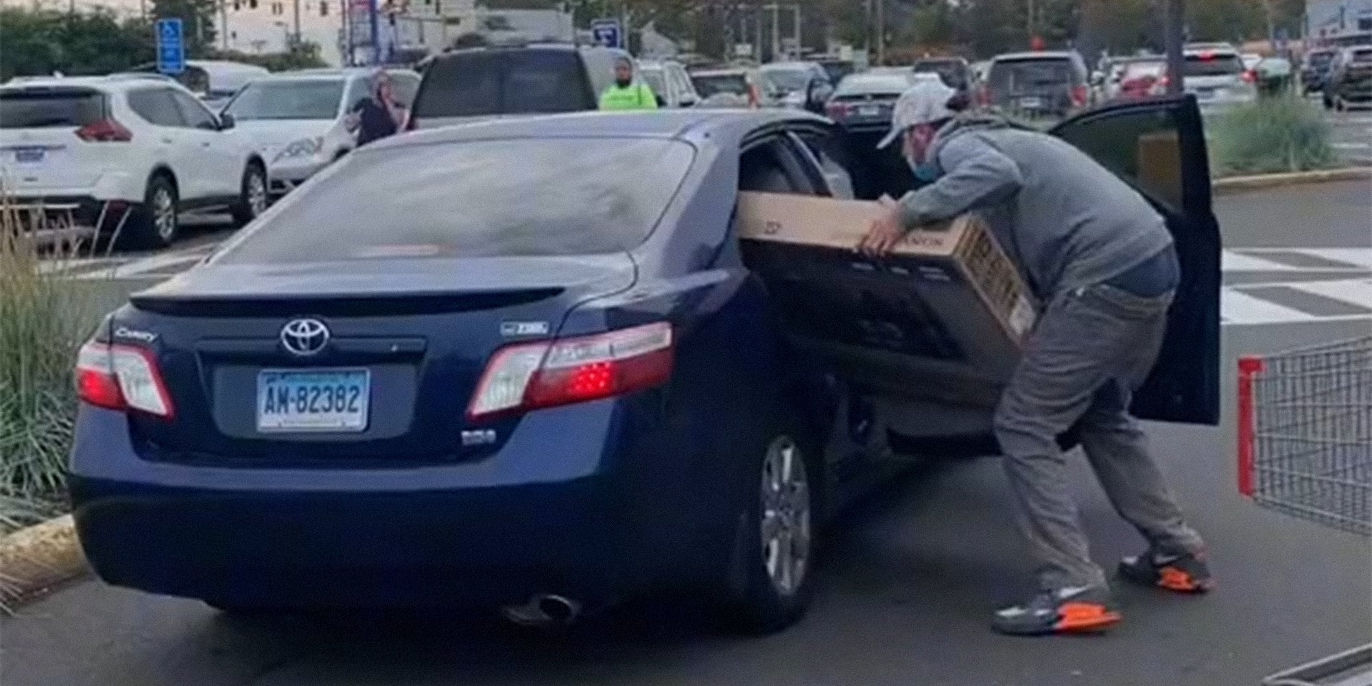 man trying to stuff television in back seat of car