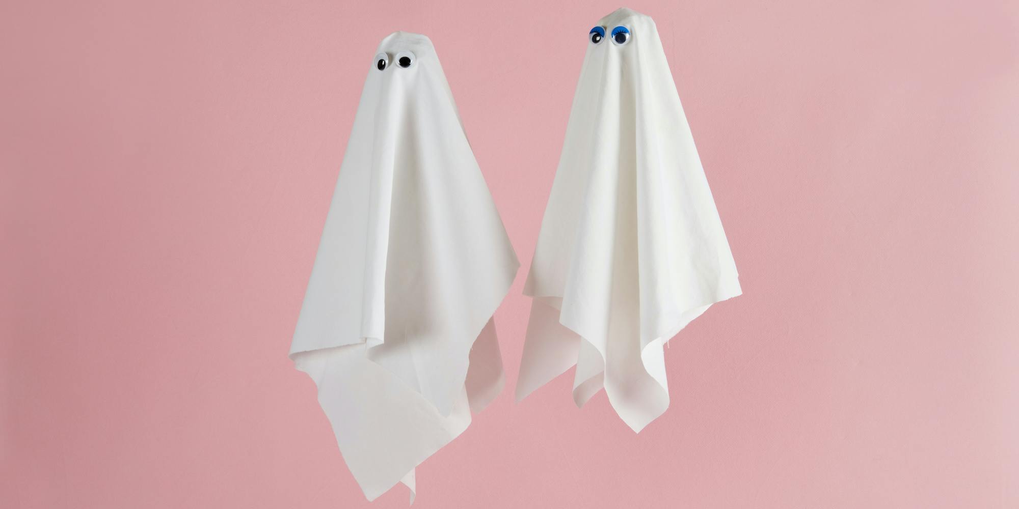 Couple of white sheet ghost with doll's eyes isolated on a pink background. Minimal pop still life photography