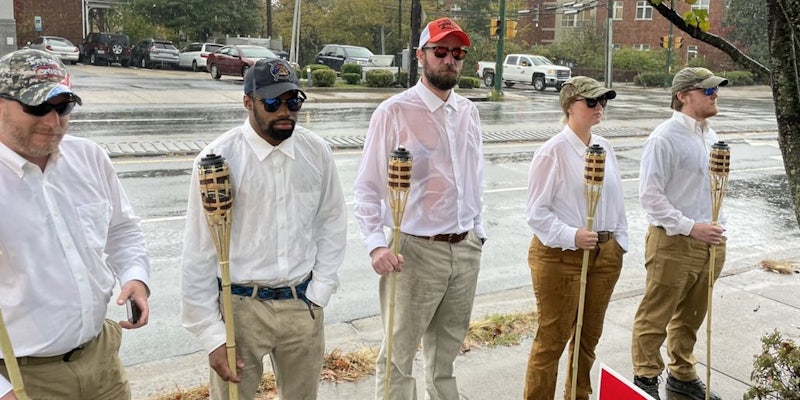 Five individuals in matching clothing holding tiki torches