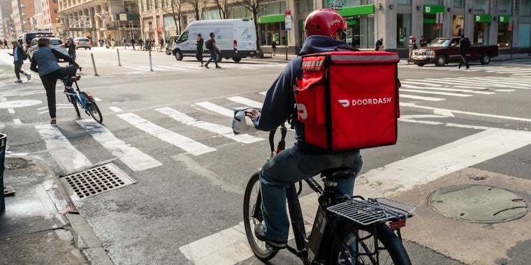 A delivery person with DoorDash riding on a bike.