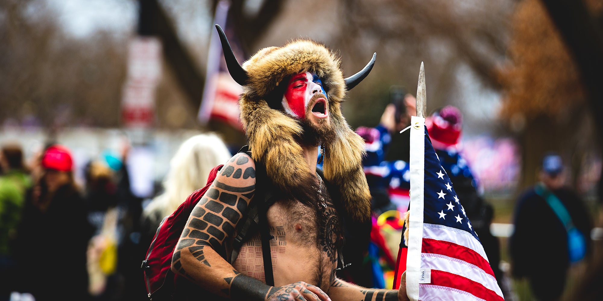 A man wearing horns and shouting in a crowd.
