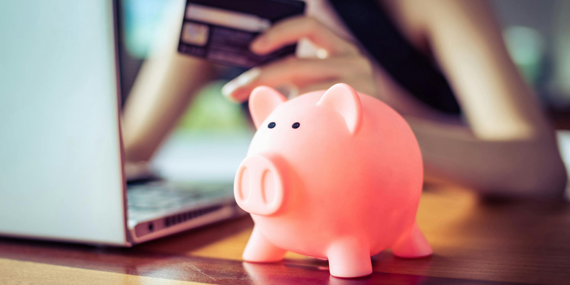 A person paying for their broadband internet service with their credit card on their laptop. In the foreground, a pink piggy bank is on the table.