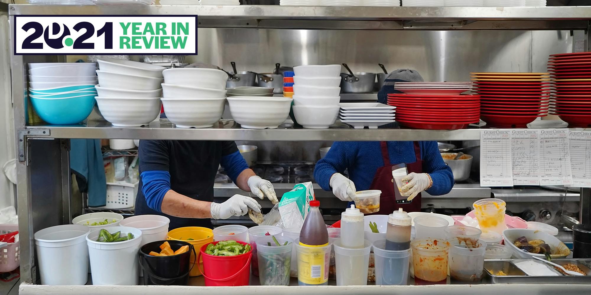 Two cooks work tirelessly behind the stacks of bowls and containers