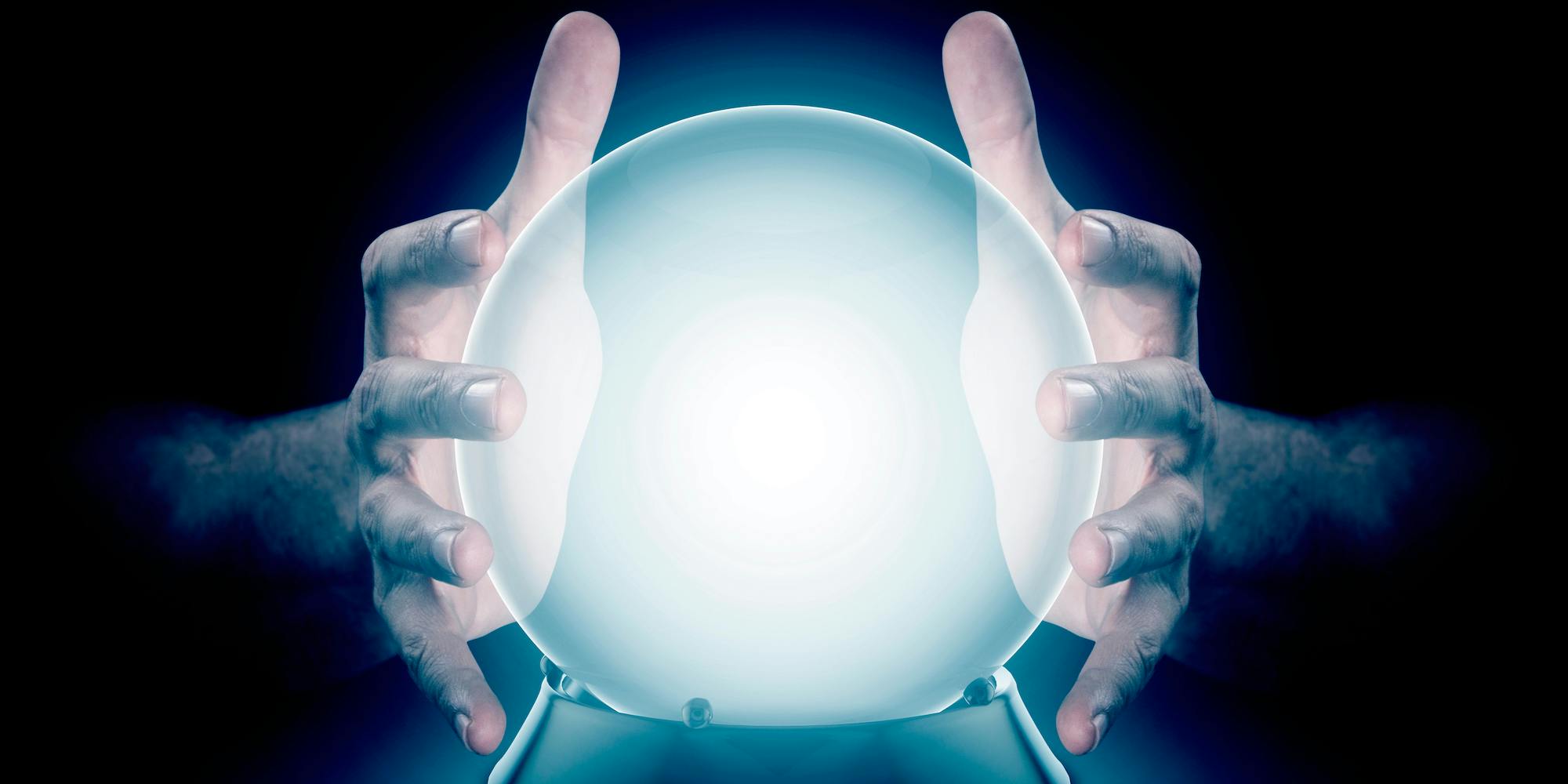 A pair of male hands surrounding a crystal ball conjuring up a hologram on an isolated dark studio background