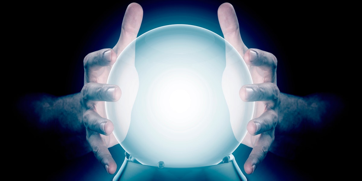 A pair of male hands surrounding a crystal ball conjuring up a hologram on an isolated dark studio background
