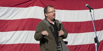 A man in front of an American flag with microphone.