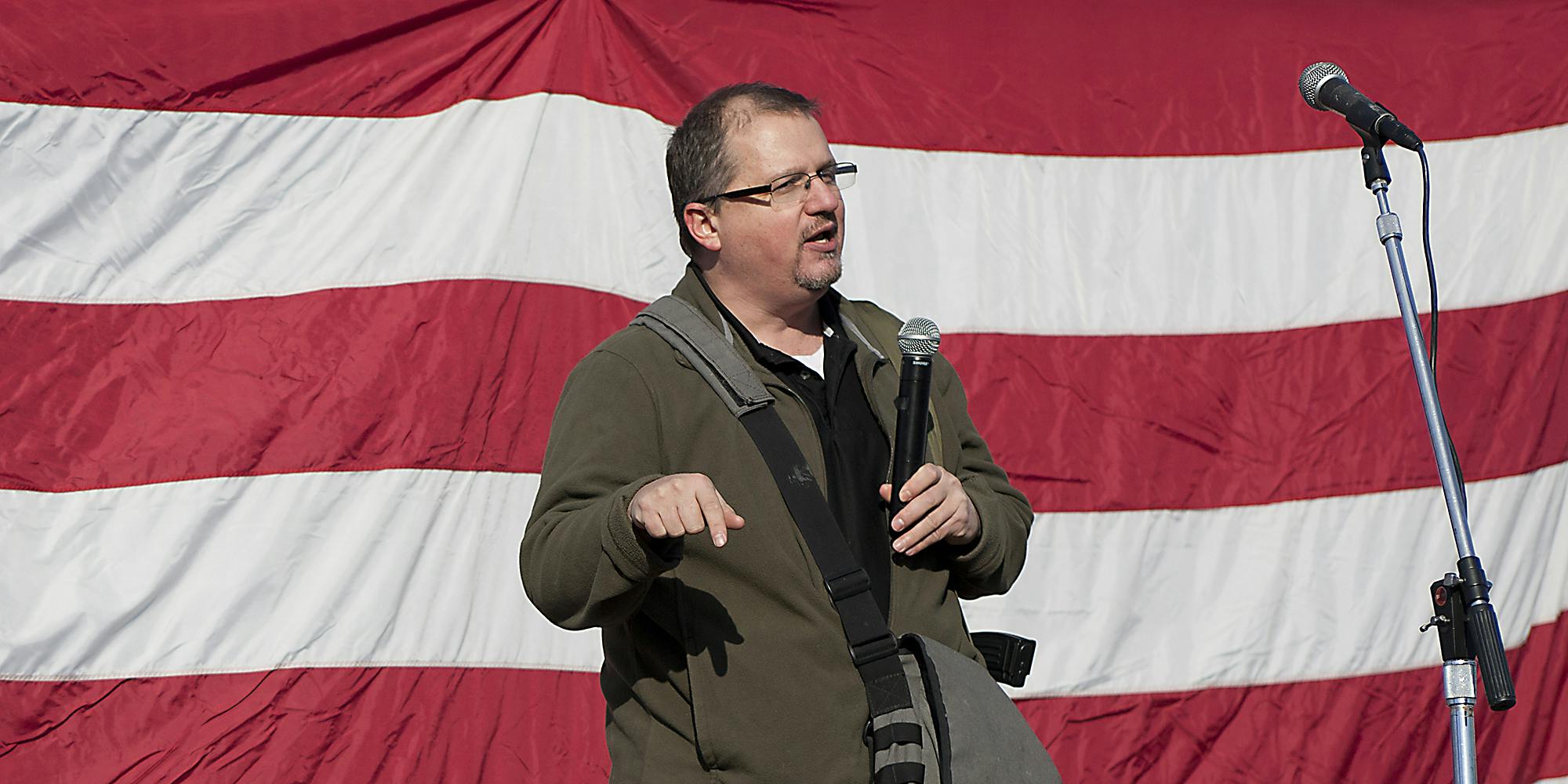  A guy in front of an American flag with microphone.