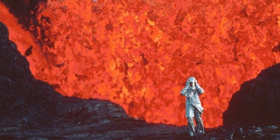 a person in silver gear standing in front of an erupting volcano in fire of love