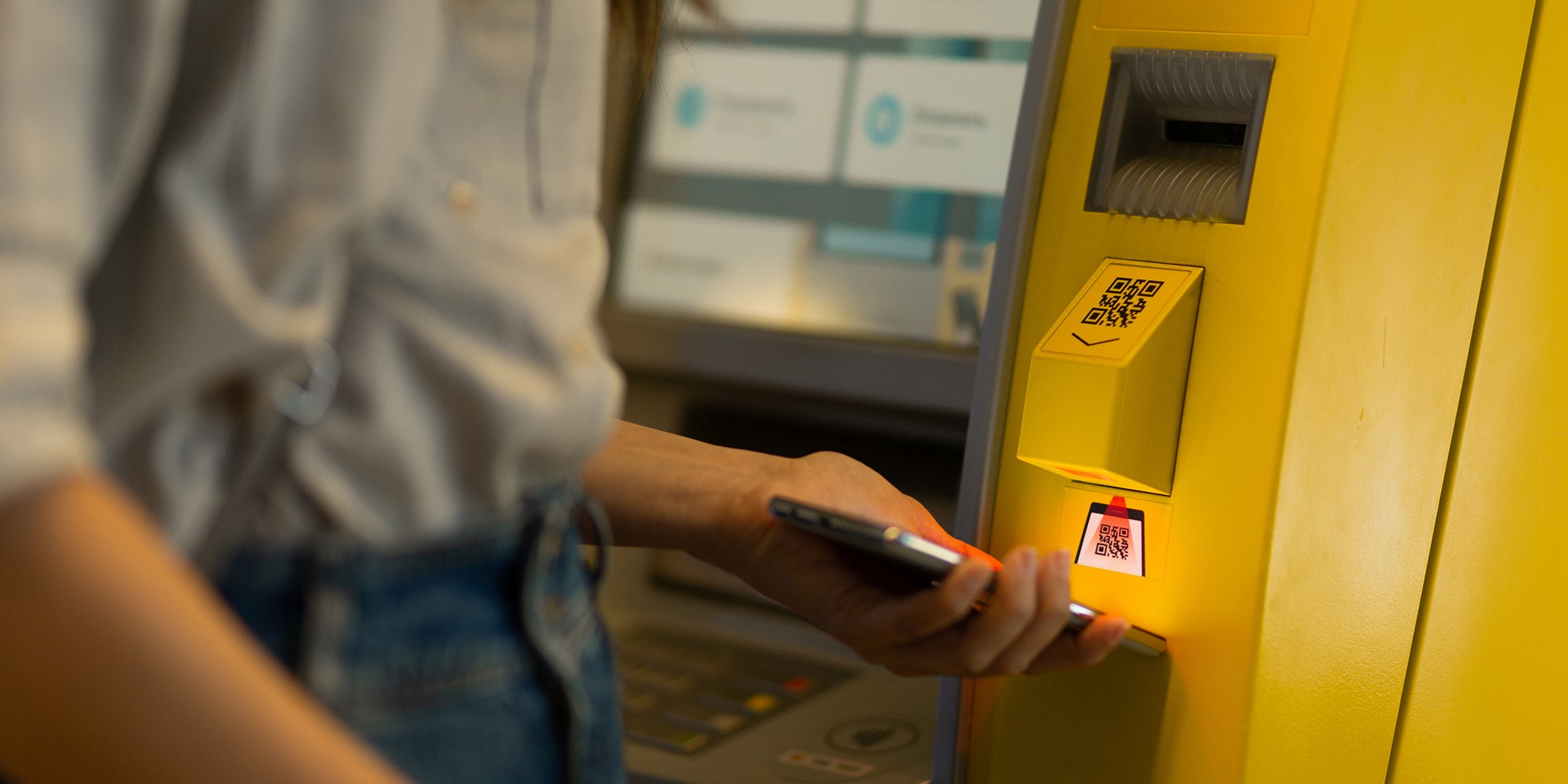 young woman scanning qr code on phone with atm