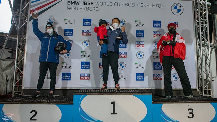 Top 3 places on stage with backdrop "BMW / IBSF World Cup Bob + Skeleton Winterberg