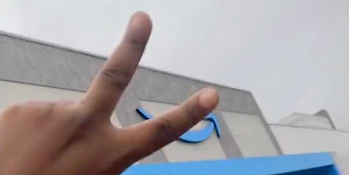 A hand giving the peace sign to an Amazon building.
