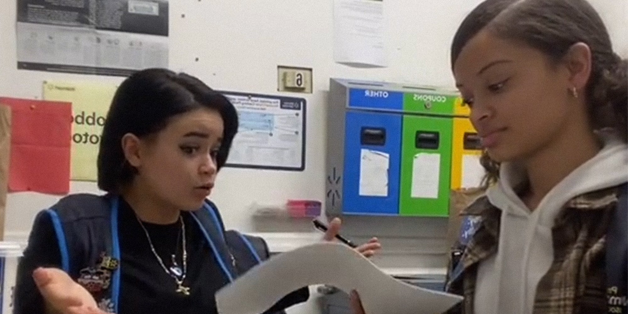 young woman shrugging while another looks at papers