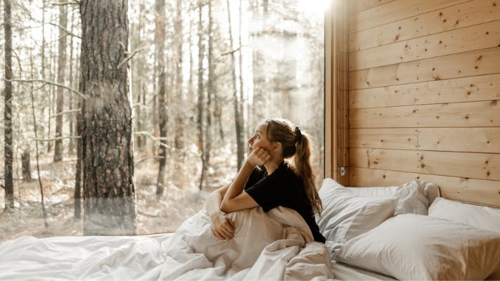 Woman sitting on bed looking outside of a large window