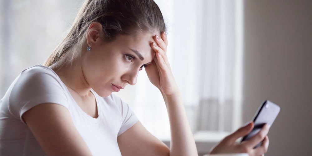 A woman looking frustrated by a robocall or scam message on her phone.