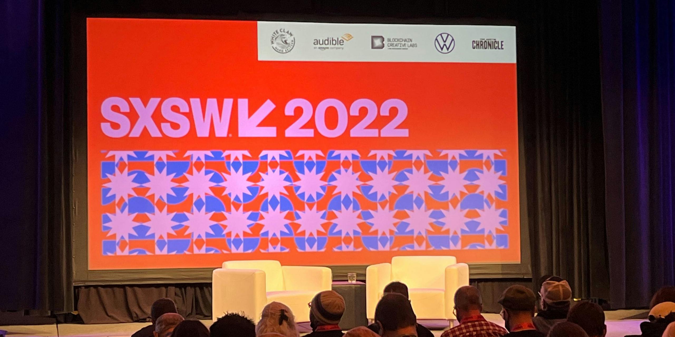 Two chairs on a stage. Behind that, a sign says 'SXSW 2022'