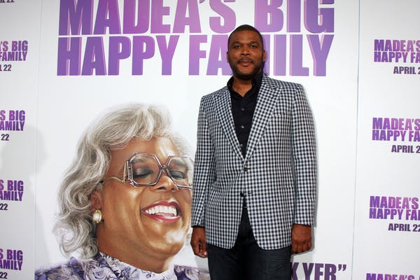 Tyler Perry on the red carpet in front of an image of Madea's Big Happy Family