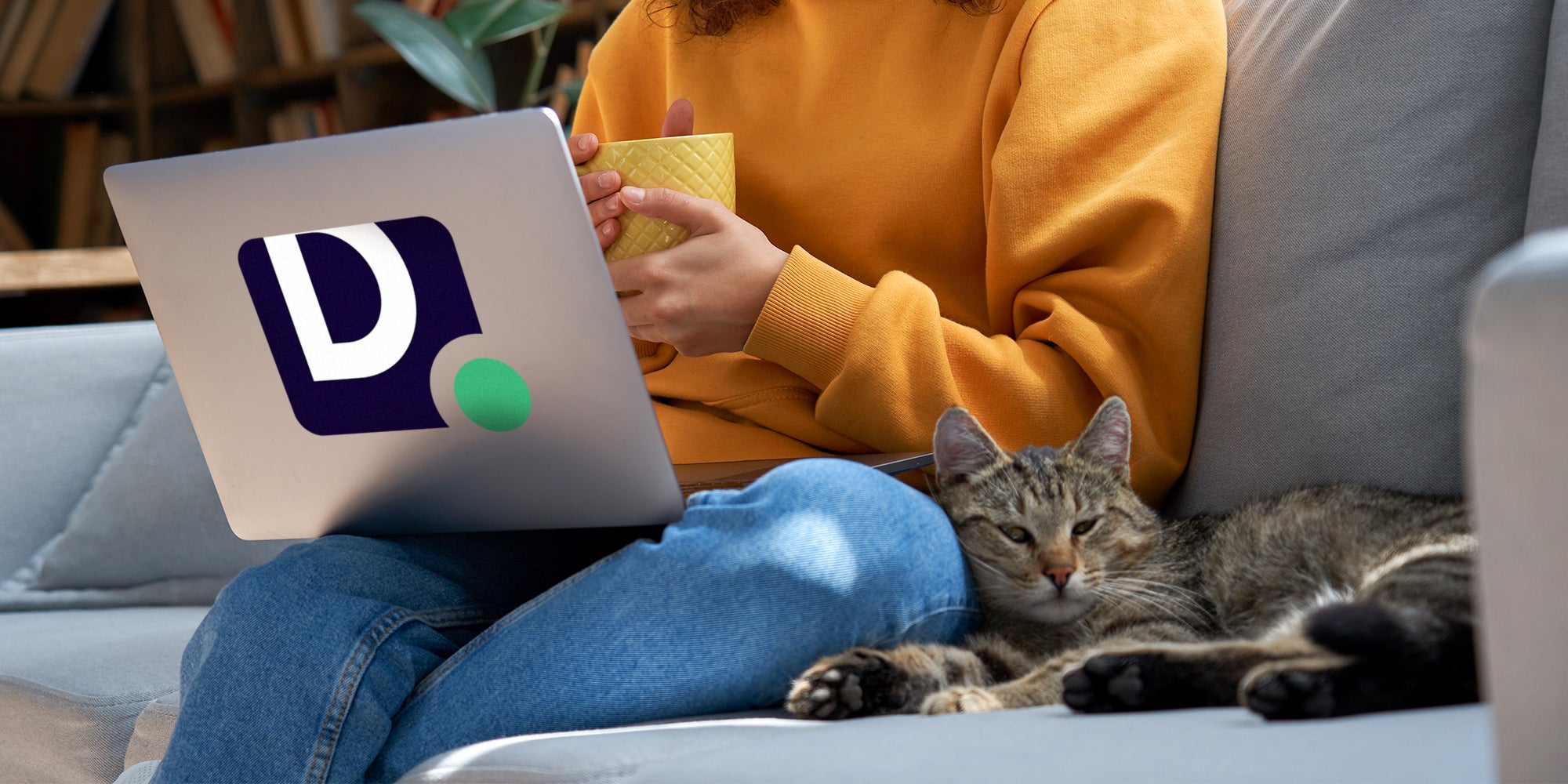 Young woman sitting near cat and holding cup while reading laptop with Daily Dot logo