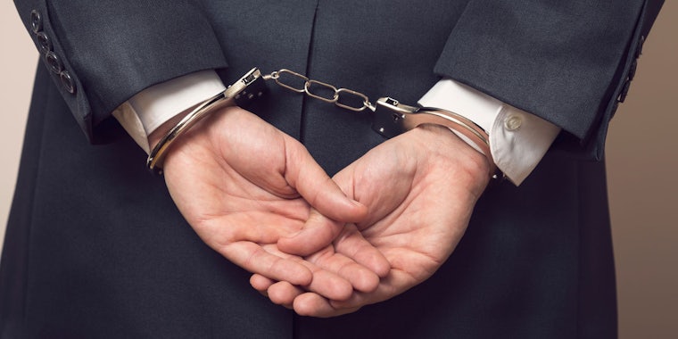 Man in business suit with hands behind his back in handcuffs