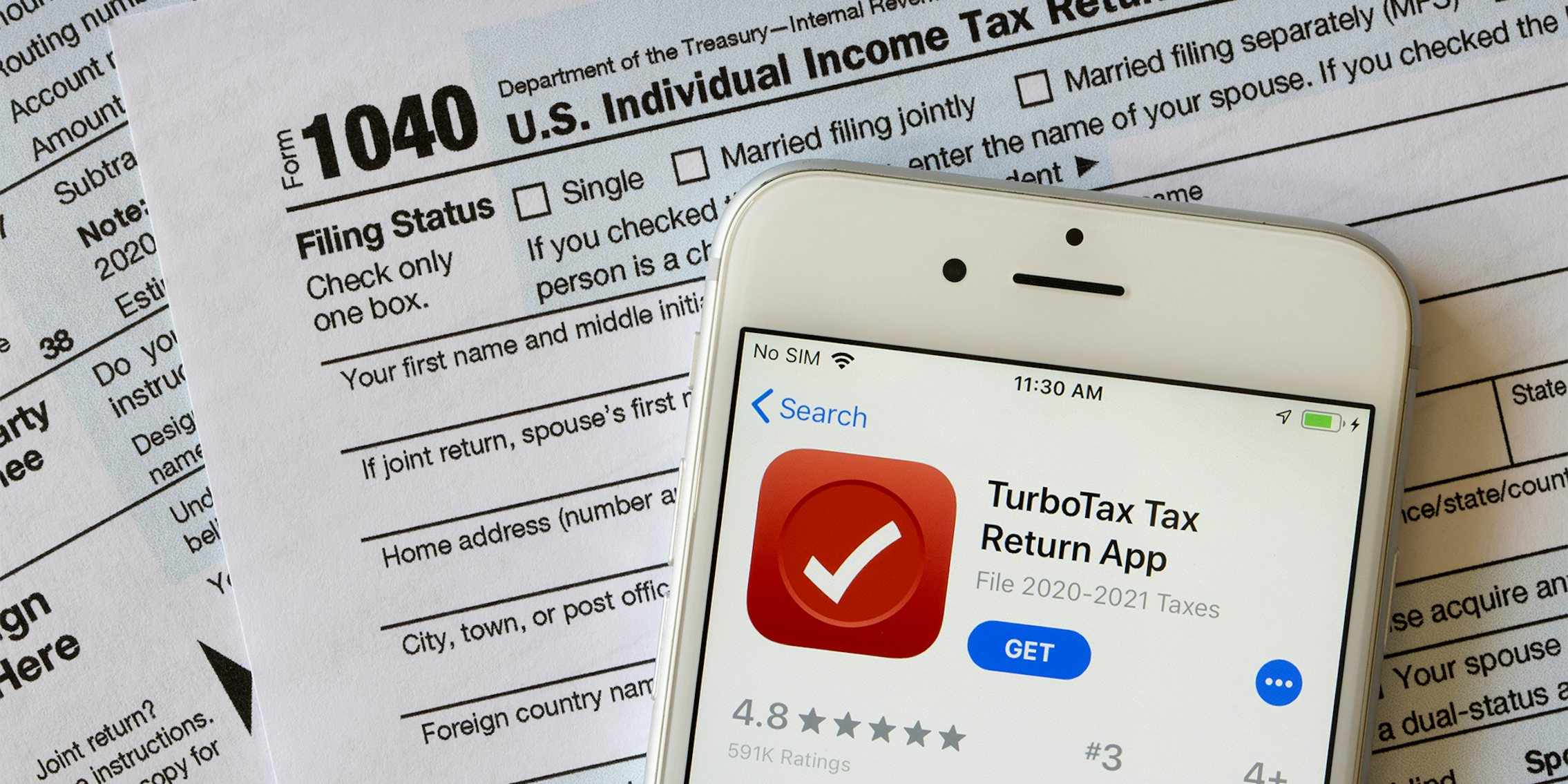 The TurboTax Tax Return App icon is seen on an iPhone atop the form 1040, U.S. Individual Income Tax Return.