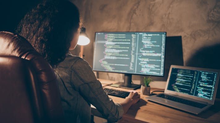 Woman sitting in front of laptop and computer screen coding