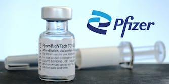 Pfizer logo with Pfizer vaccine in bottle and syringe behind (blurred) on table with light blue background