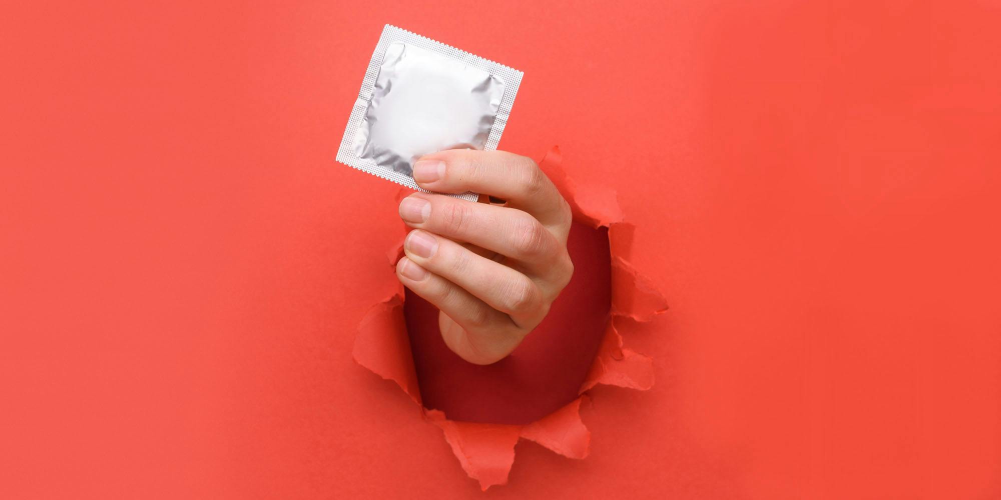 hand popping out of red paper background handing condom out