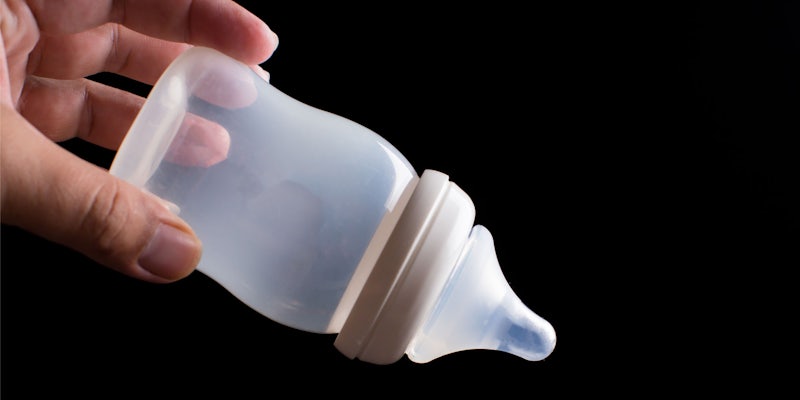 man hand holding empty baby bottle tipped down on black background