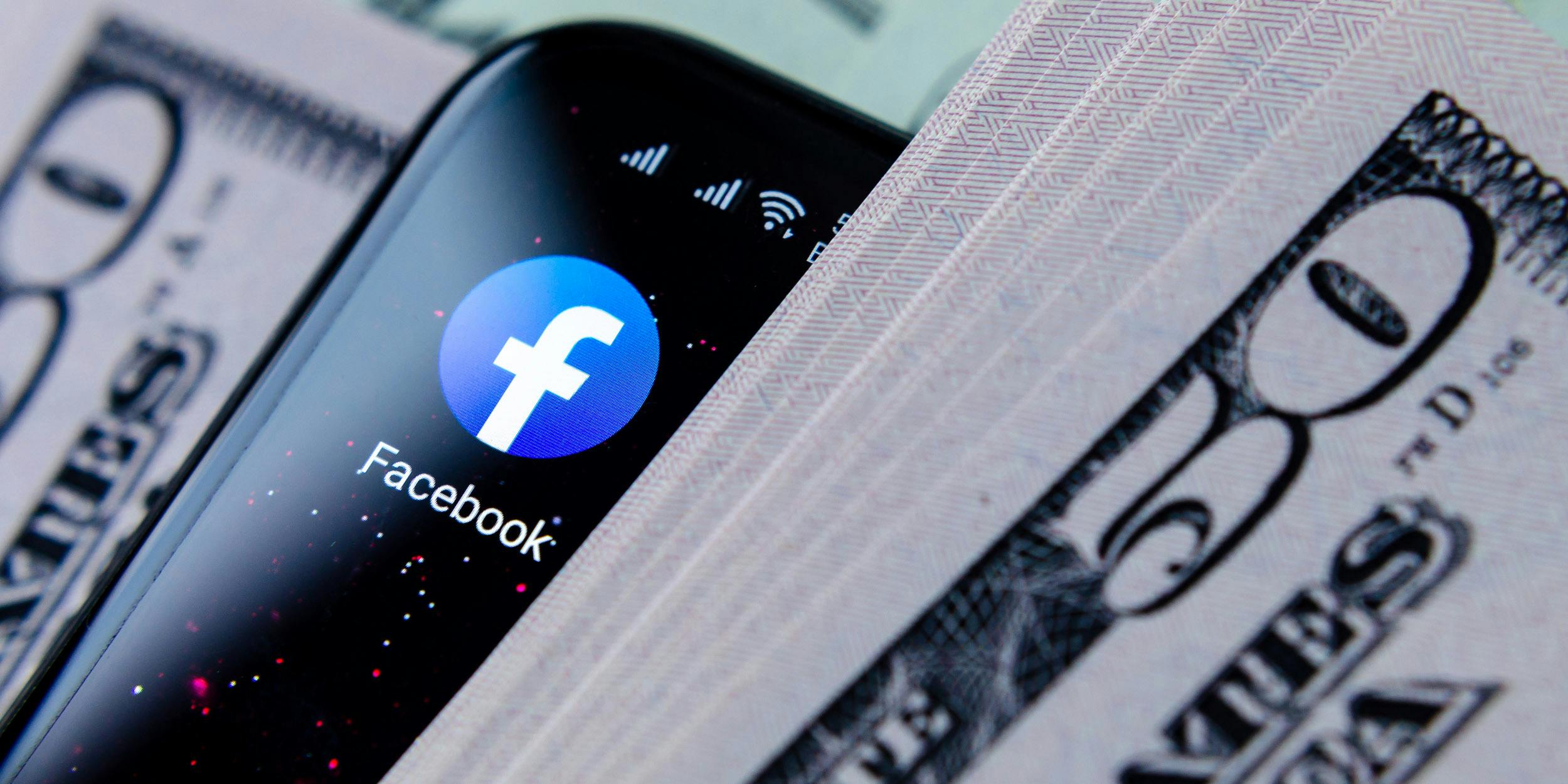 A smartphone showing the Facebook app in between stacks of $50 bills.