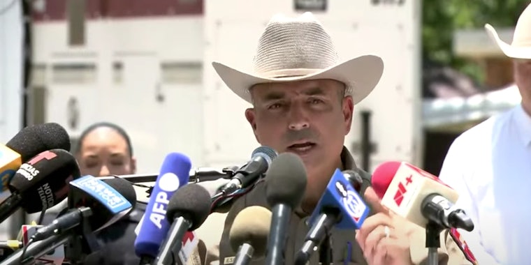 A man in a cowboy hat speaking into numerous microphones