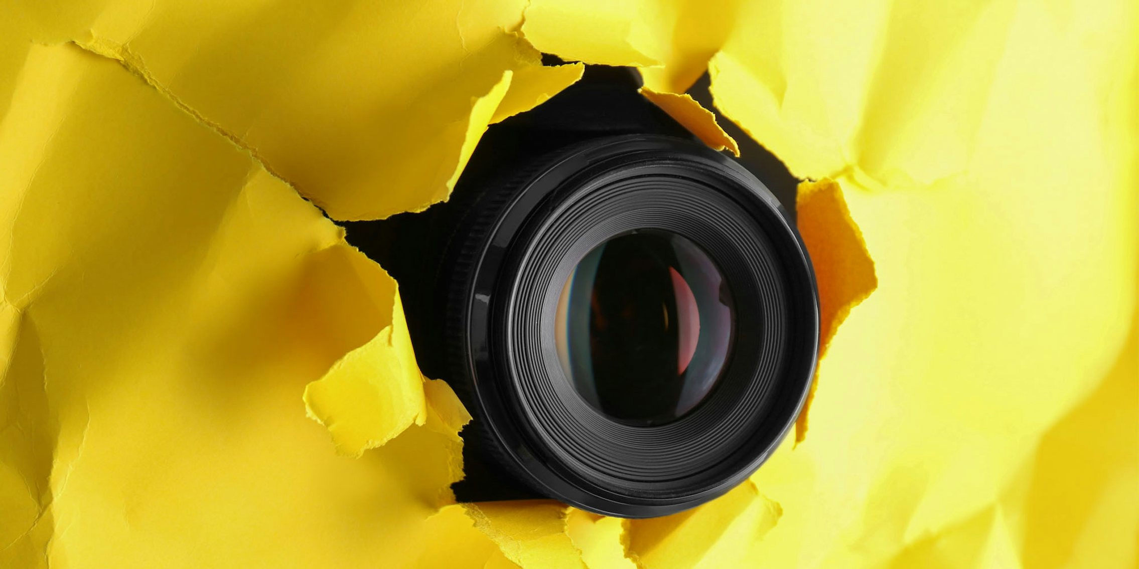 Camera lens popping through yellow paper