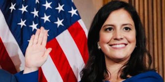 Rep. Elise Stefanik with hand up and American flag behind her