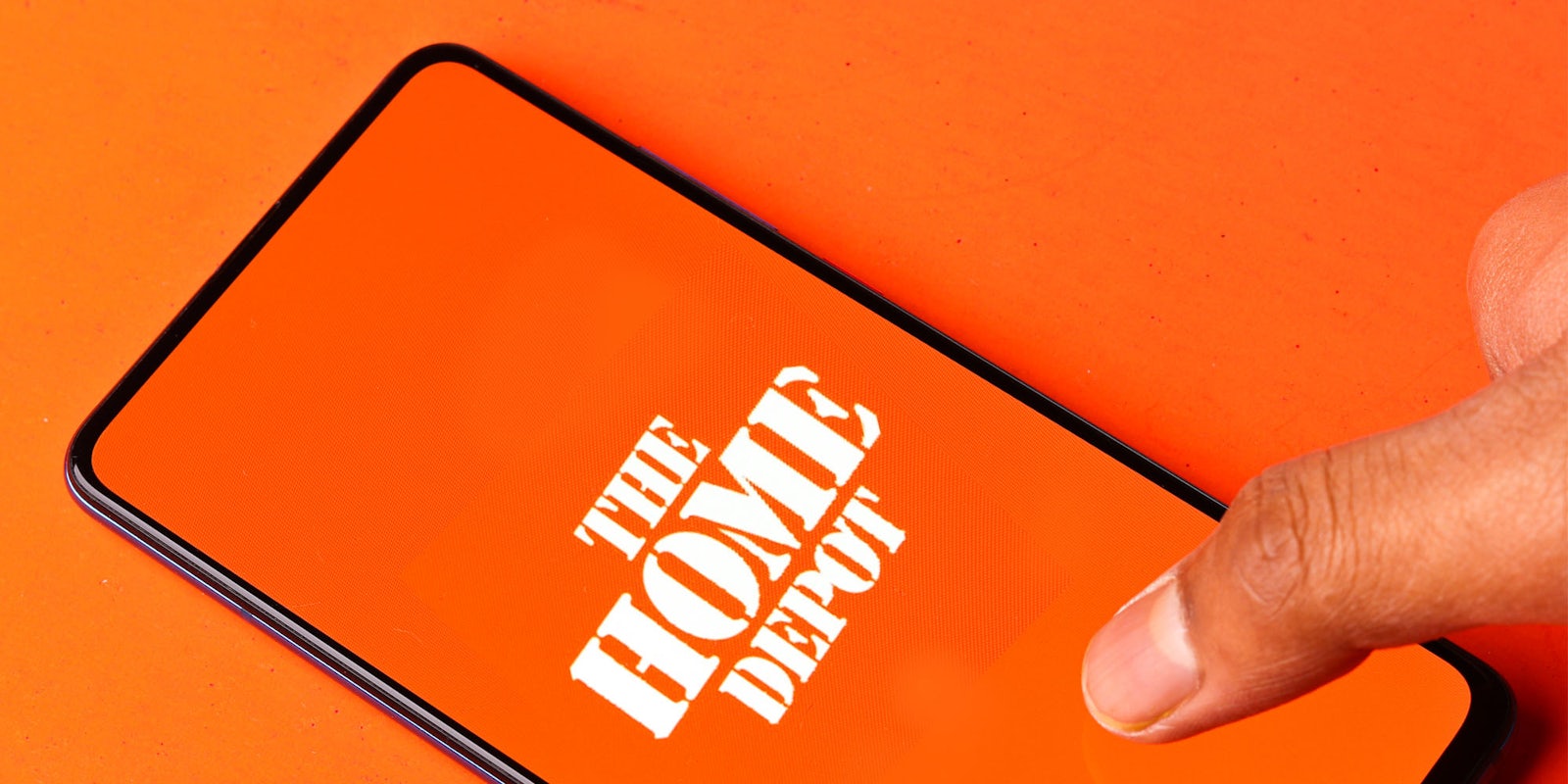 finger on phone screen that has The Home Depot logo white centered, orange background