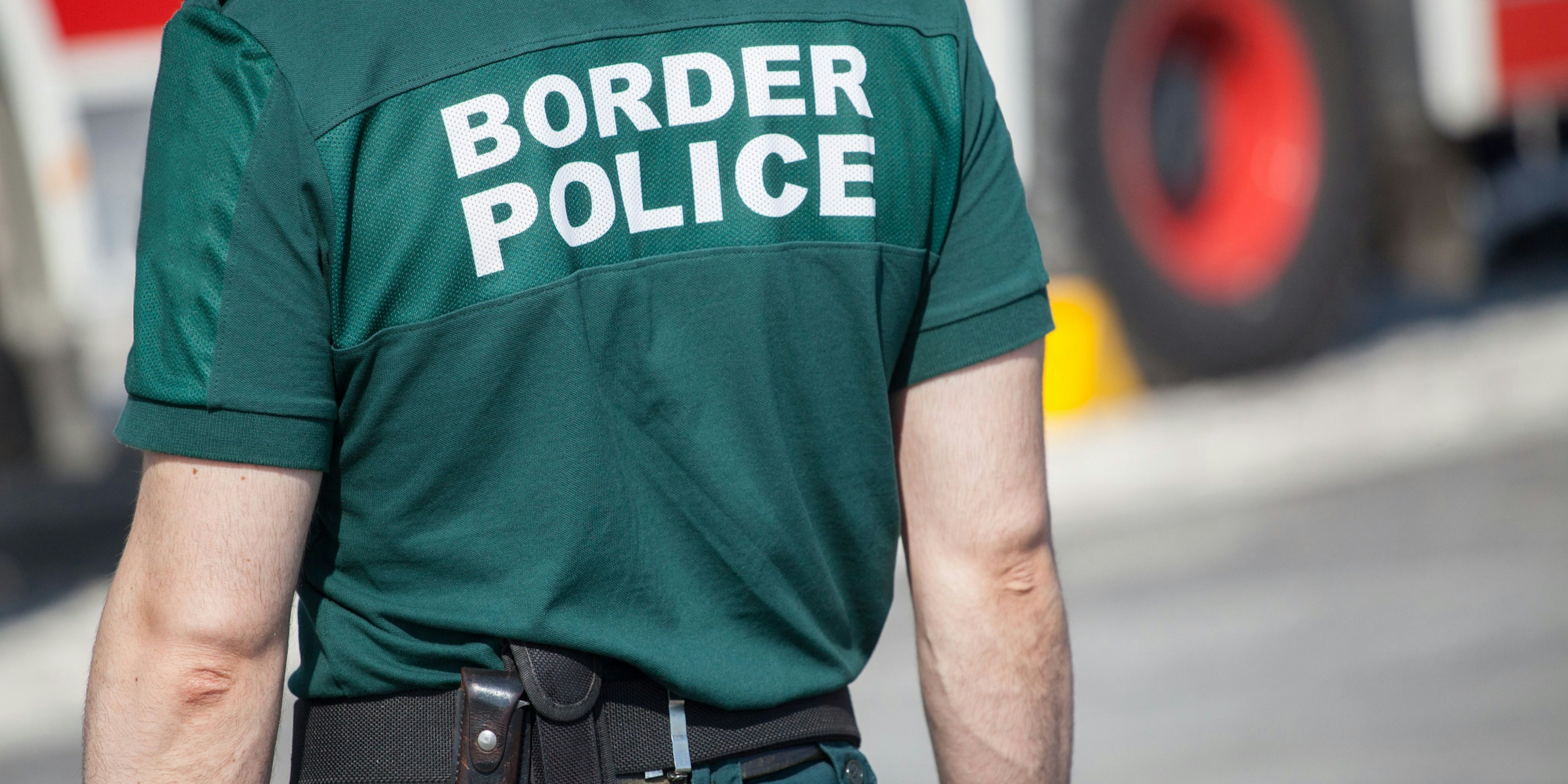 Person facing away from camera, wearing green Border Police shirt