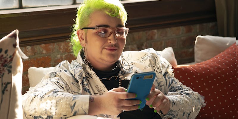 A genderqueer person looking at their phone