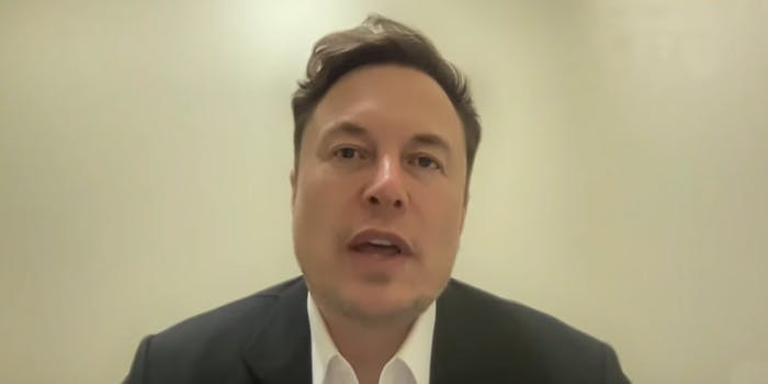 Elon Musk speaking on tan background