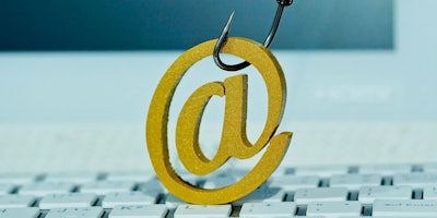 golden @ symbol hanging on fish hook phishing concept keyboard underneath computer screen blurred in background