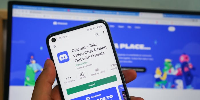 Man holding smartphone opens Discord app on smartphone with Discord logo.