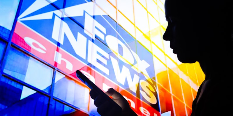 silhouette holds a smartphone with the Fox News Channel logo in the background