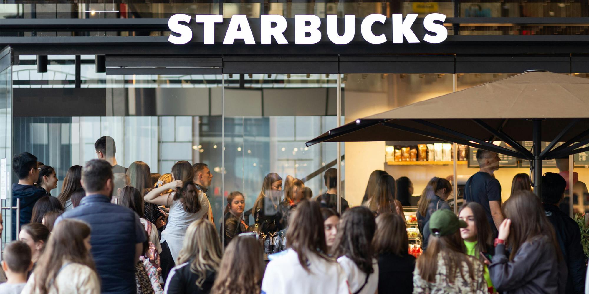 Starbucks building with sign customers in large group in line waiting