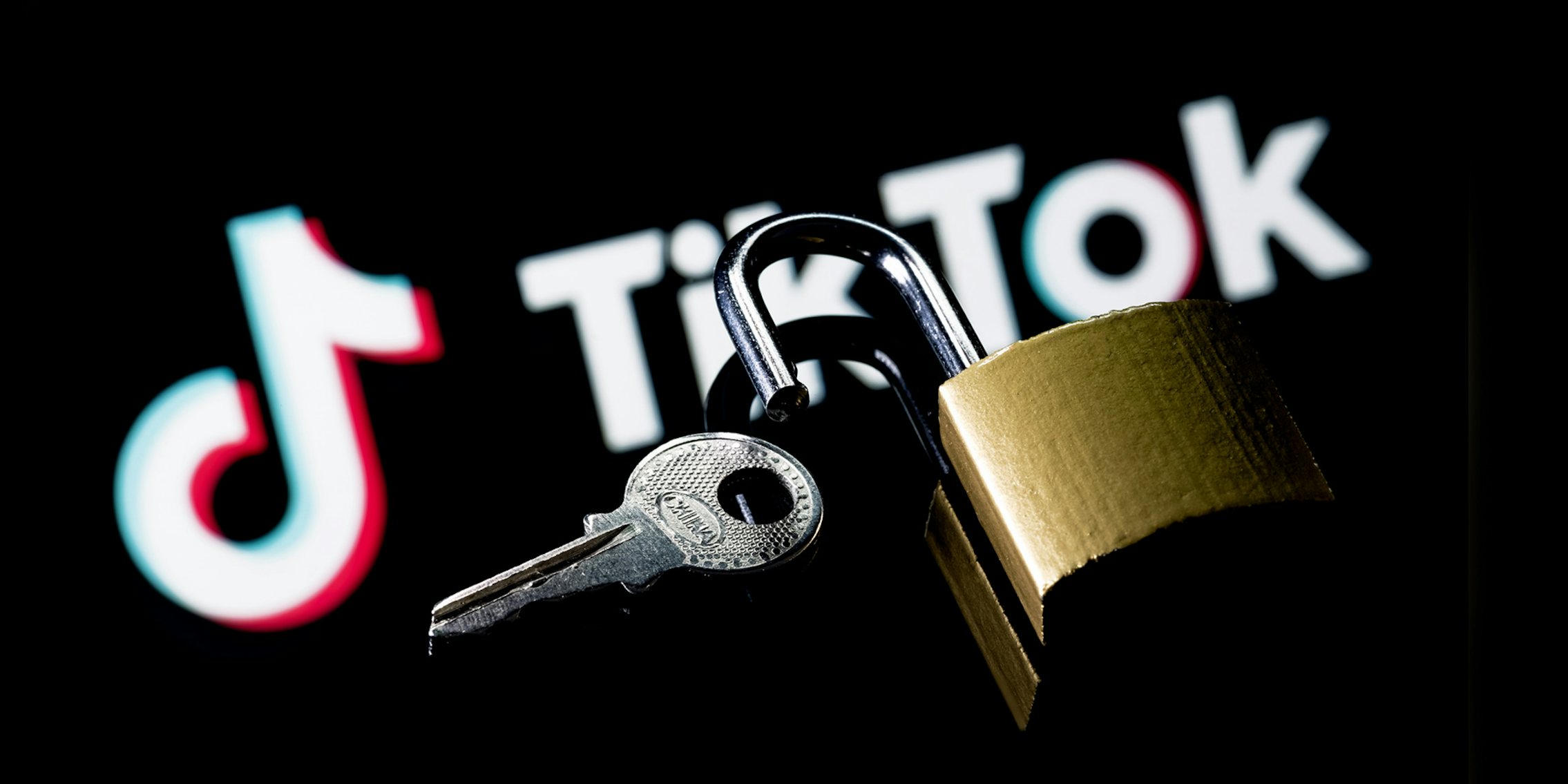 TikTok logo blurred underneath open lock with key on black background