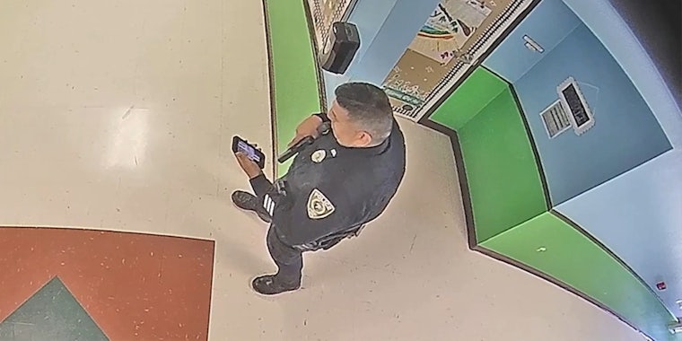 police officer with gun drawn looks at phone screen with punisher skull flag logo