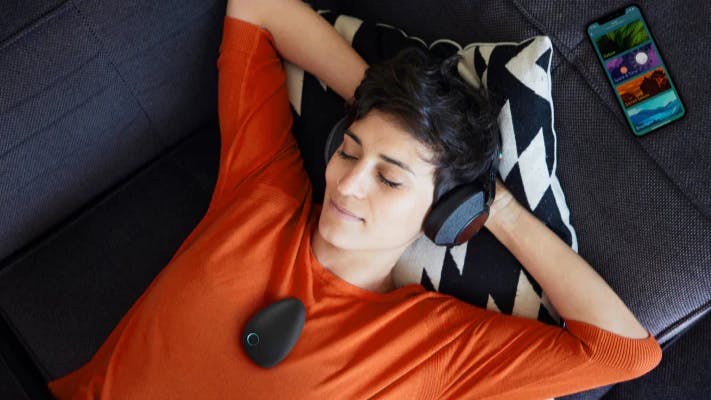 Woman relaxing on couch with headphones using Sensate wellness tech